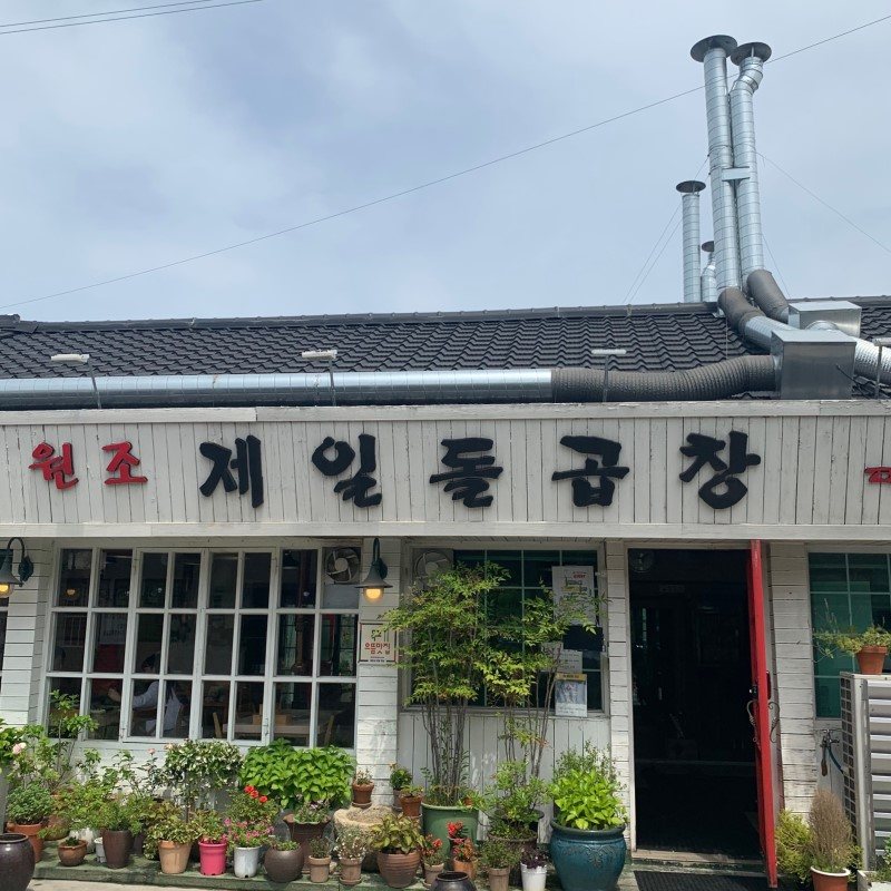 기와지붕 아래 흰 판자벽에 ‘원조 제일돌곱창’ 간판을 단 목포 본점. 붉은 문틀 입구 앞에 화분이 가득하다