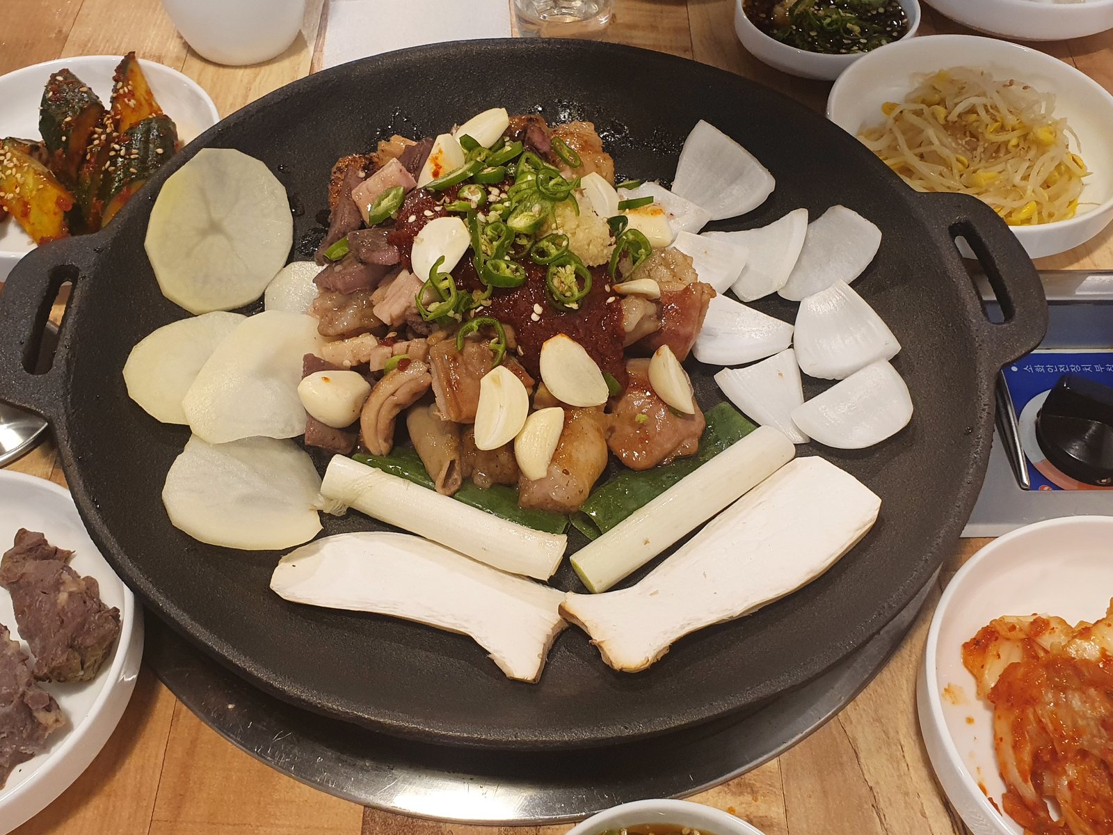 제일돌곱창 상무점의 한우양념모듬구이 — 둥근 판 가운데 양념한 곱창·대창·염통에 청양고추와 통마늘을 올리고 둘레에 감자·양파·대파·새송이를 둘렀다